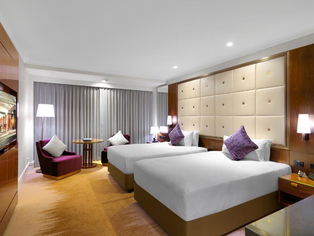 Amora Hotel Jamison Sydney Ngoại thất bức ảnh The photo shows a modern hotel room featuring two beds with white sheets and purple accent pillows. There is a stylish headboard behind the beds, and the room is well-lit with lamps on bedside tables. A seating area includes a purple chair and a smal