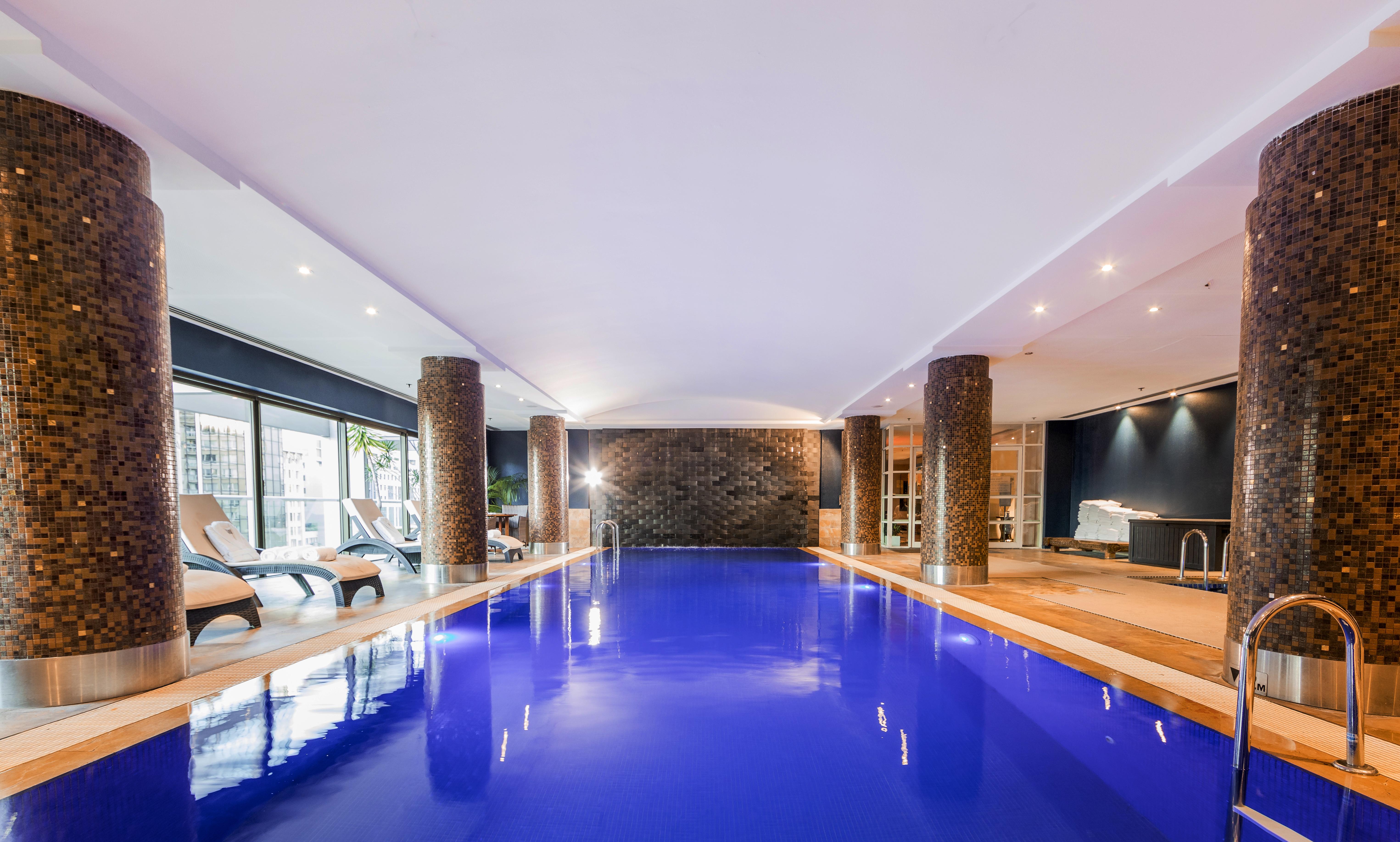 Amora Hotel Jamison Sydney Ngoại thất bức ảnh The photo shows an indoor swimming pool. The water is a striking blue color, and the surrounding area has modern decor. There are stone columns supporting the ceiling, and the lighting is bright and inviting. To one side, there are several lounge cha