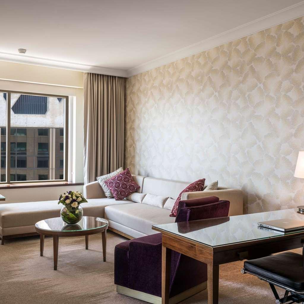 Amora Hotel Jamison Sydney Phòng bức ảnh The photo depicts a modern and stylish living area. It features a light-colored sofa with decorative cushions, a coffee table in the center, and a desk with a chair. The walls are adorned with a patterned wallpaper, and there are large windows lettin