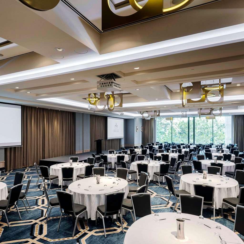 Amora Hotel Jamison Sydney Tiện nghi bức ảnh The photo shows a spacious conference or banquet room set up for an event. It features multiple round tables with white tablecloths and black chairs arranged neatly throughout the room. There are two screens positioned at the front, likely for presen