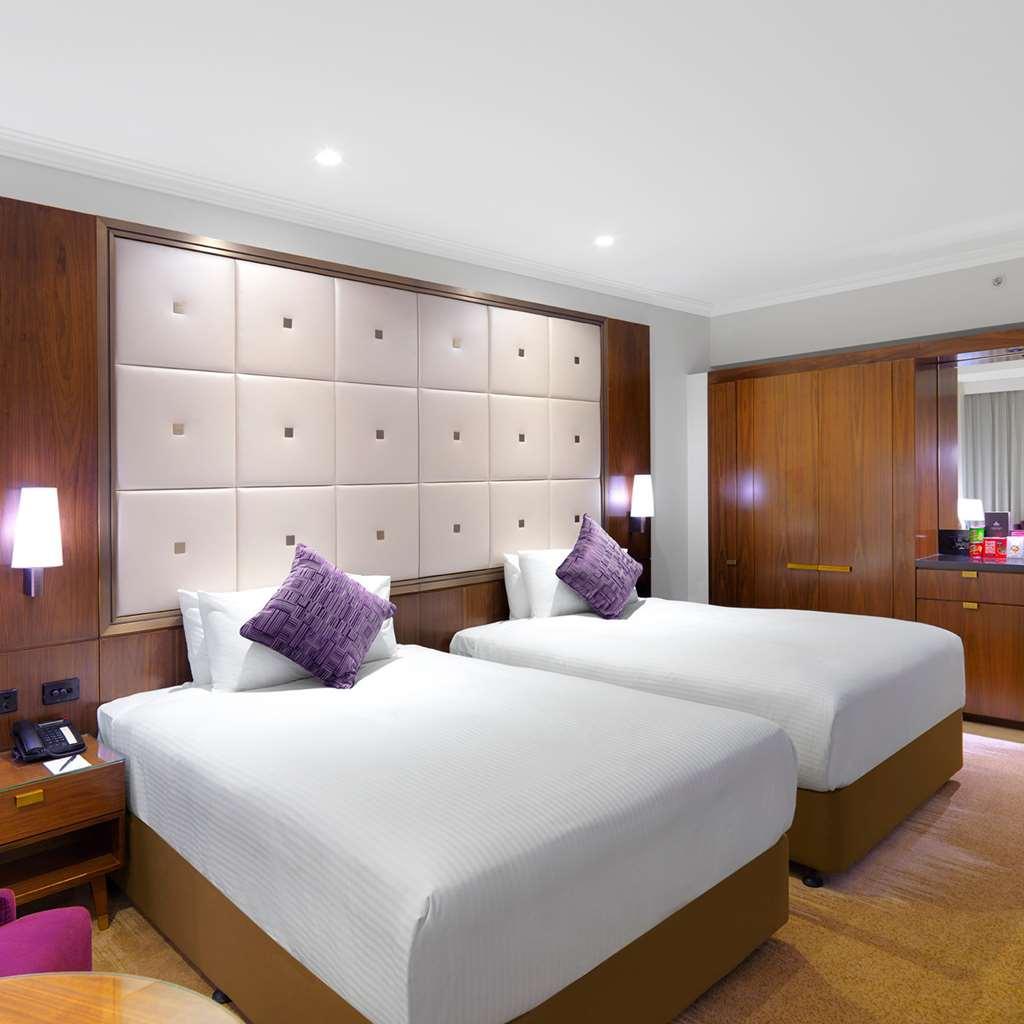 Amora Hotel Jamison Sydney Phòng bức ảnh The photo depicts a hotel room featuring two twin beds with white beddings. Each bed is accented by a purple decorative pillow. The room has a modern design, with a large upholstered headboard that has a grid pattern. There are warm wooden elements i
