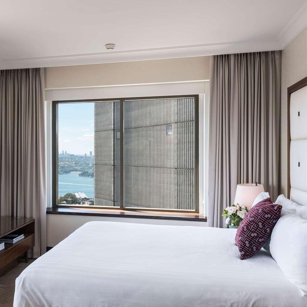 Amora Hotel Jamison Sydney Phòng bức ảnh The photo shows a modern hotel room with a large window that offers a view of the outside. The room features a neatly made bed with white bedding and a decorative pillow. There are light-colored curtains framing the window, which appears to overlook 