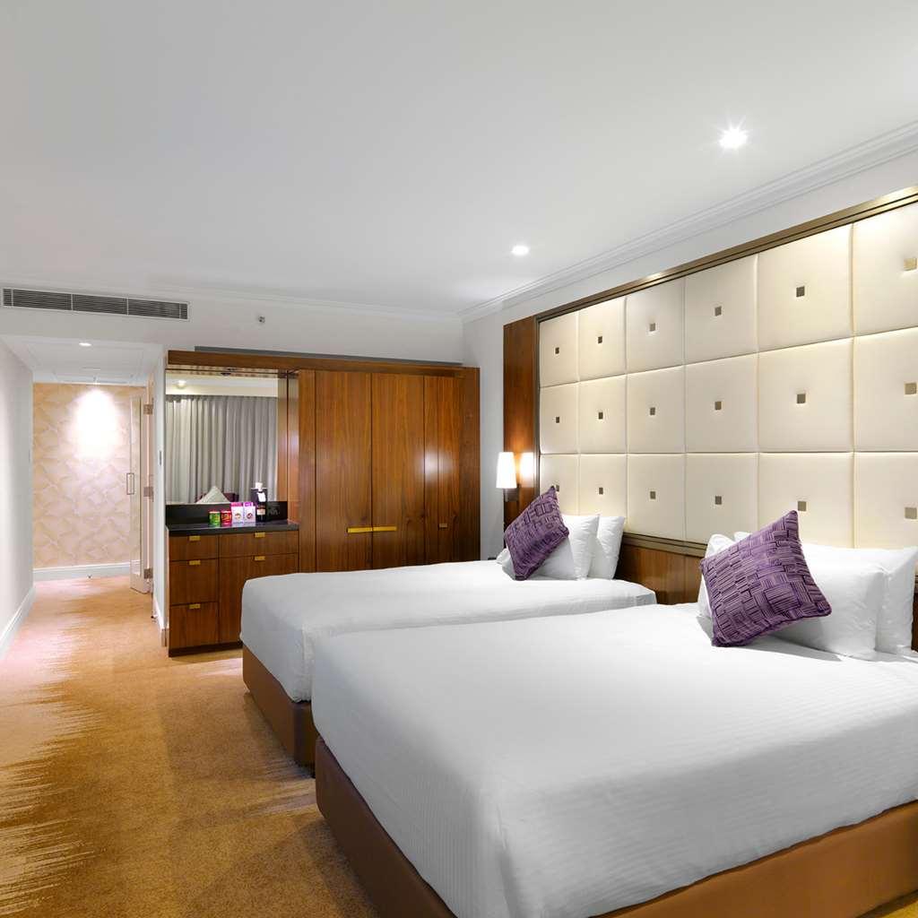 Amora Hotel Jamison Sydney Phòng bức ảnh The photo shows a modern hotel room featuring two twin beds with white bedding and purple decorative pillows. The walls are designed with soft beige panels, creating a luxurious ambiance. There’s wooden furniture, including a cabinet against one wall
