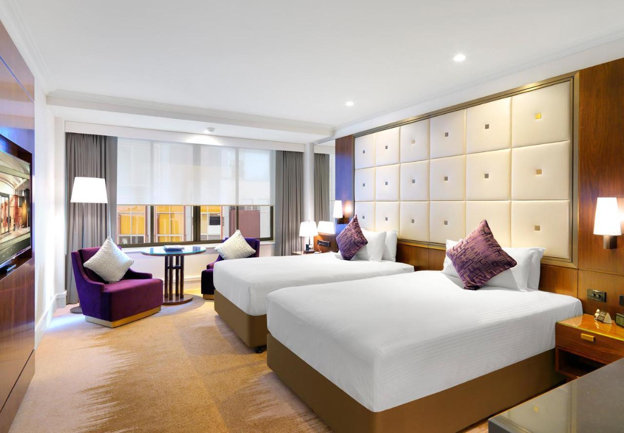 Amora Hotel Jamison Sydney Ngoại thất bức ảnh The photo shows an elegant hotel room featuring two beds with white linens and decorative pillows. The beds are positioned against a stylish headboard with a soft, padded design. There’s a cozy seating area with a purple armchair and a small round ta