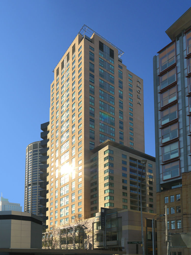 Amora Hotel Jamison Sydney Ngoại thất bức ảnh The photo shows a tall building with a modern architectural design, featuring a mix of glass and concrete materials. The building is predominantly light-colored with large windows reflecting sunlight. It appears to have multiple floors, and the name 