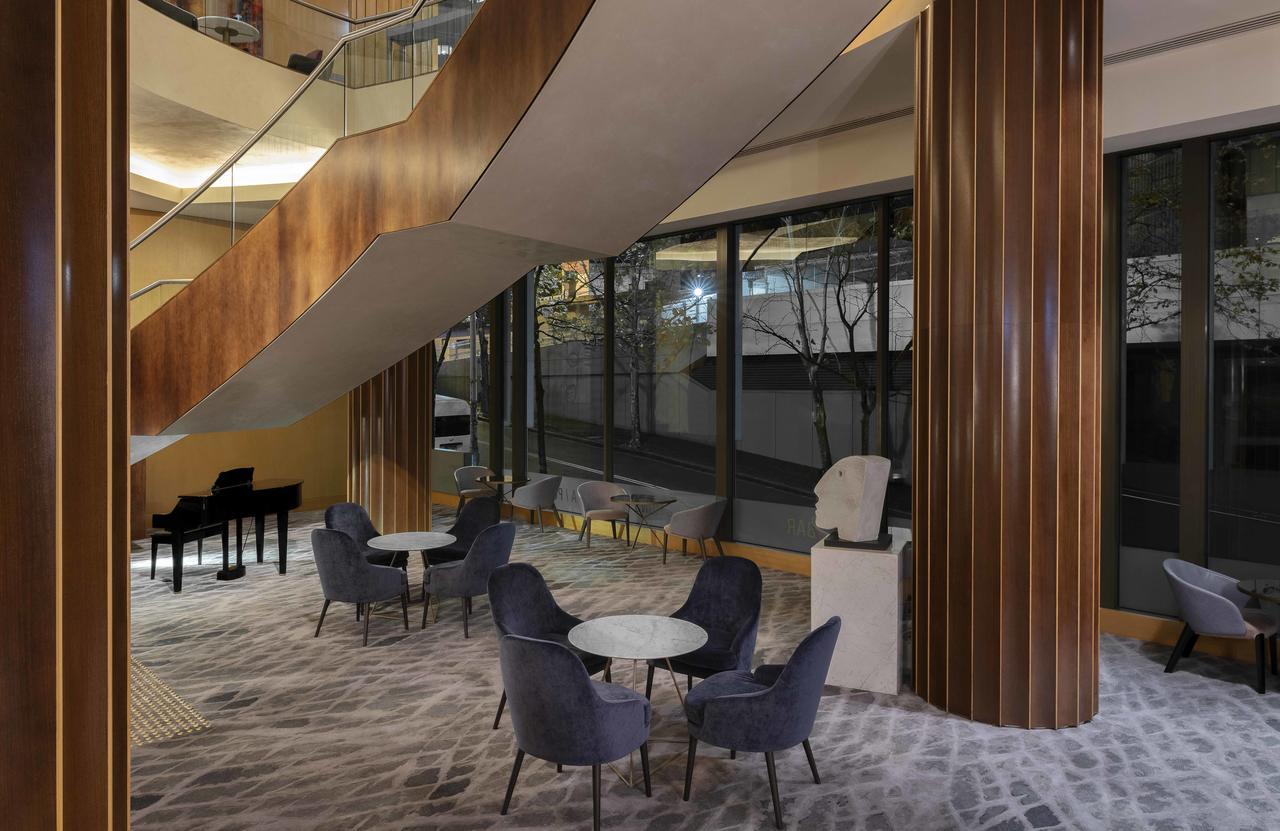 Amora Hotel Jamison Sydney Ngoại thất bức ảnh The photo depicts a modern interior space featuring a stylish lounge area. There are several comfortable chairs and small tables arranged on a patterned carpet. A large staircase with a sleek design is visible, leading to an upper level. The area is 