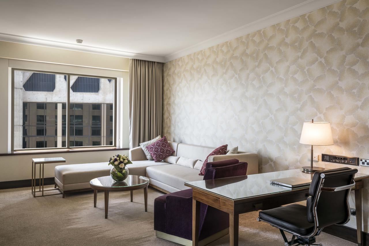 Amora Hotel Jamison Sydney Ngoại thất bức ảnh The photo shows a modern hotel room or a stylish living area. There is a comfortable white sofa with decorative pillows arranged in a cozy seating area. A glass coffee table with a small floral arrangement is positioned in front of the sofa. To the r