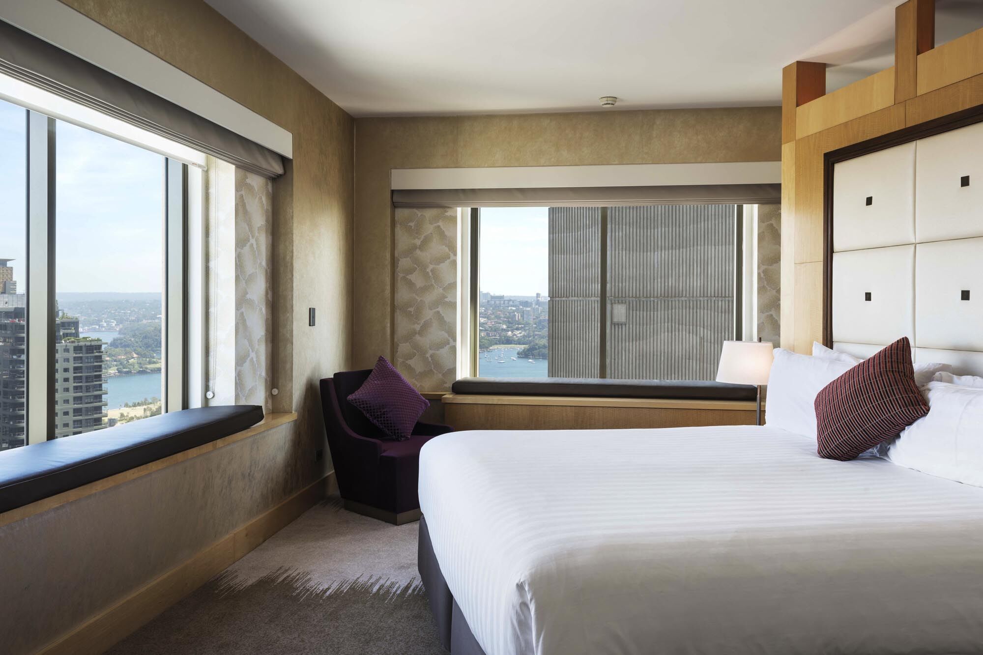Amora Hotel Jamison Sydney Ngoại thất bức ảnh The photo shows a modern, stylish hotel room featuring a bed with white linens, a decorative pillow, and a cozy chair with a purple cushion. Large windows provide a view of the outside scenery, which appears to include a body of water and buildings. 