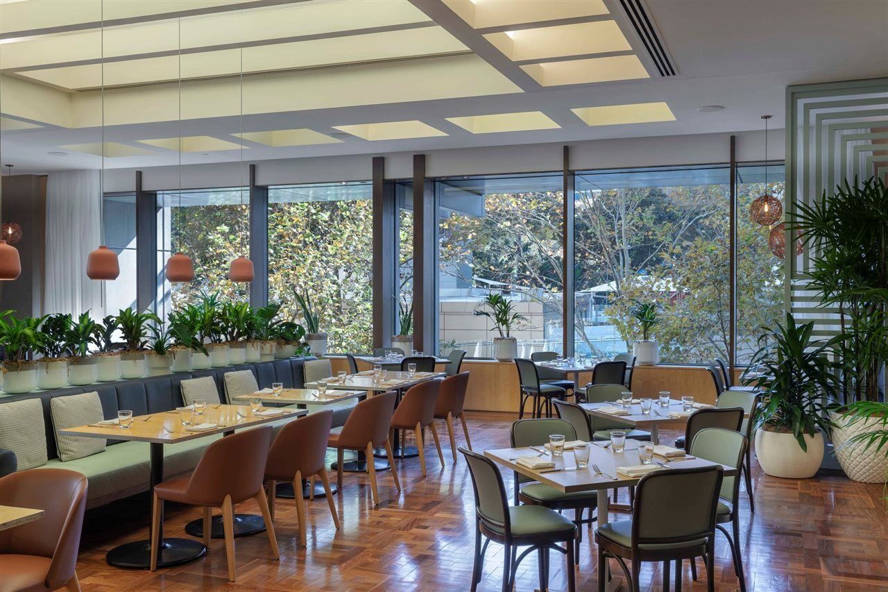 Amora Hotel Jamison Sydney Ngoại thất bức ảnh The photo shows a modern restaurant interior characterized by a spacious layout with large windows allowing natural light to fill the room. There are several dining tables arranged throughout the space, some set for meals with dishes and utensils, wh