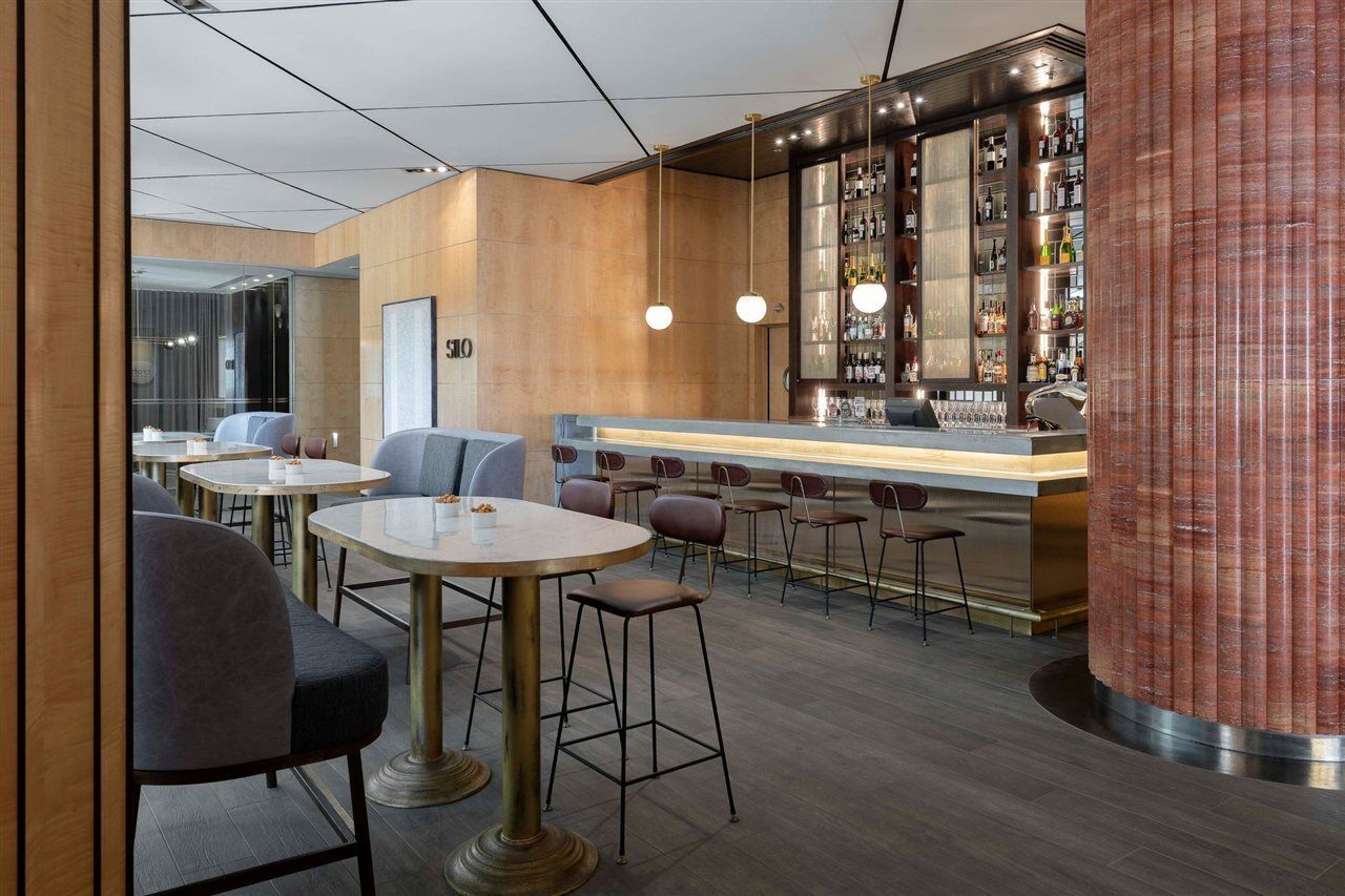 Amora Hotel Jamison Sydney Ngoại thất bức ảnh The photo shows a modern interior of a bar or lounge area. There are several tables with chairs, featuring round and rectangular tops, and a mix of seating styles, including higher bar stools and lower chairs. The bar itself is well-lit, with a sleek